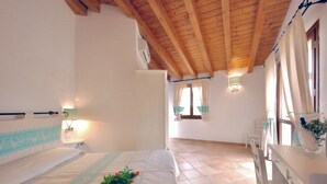 Un dormitorio con techo de madera, una cama con cabecera decorativa, una mesita de noche y una ventana con cortinas.