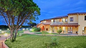 Una casa de dos pisos con techo de tejas, césped cuidado y un gran árbol en primer plano.