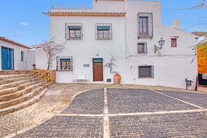 A white building with a cobblestone courtyard, a wooden door, and a sign that reads 'CAJOTEXM.'