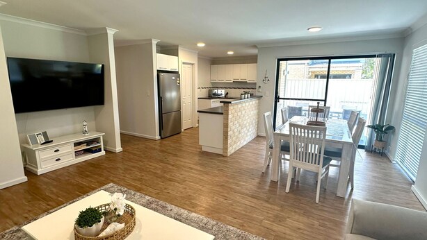 Una cocina moderna con una isla central, un comedor con mesa de vidrio y una sala de estar con televisor de pantalla plana.