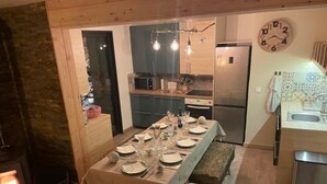 Ein gemütlicher Essbereich mit einem Tisch für vier Personen, einer Bank, einem Kamin, einer Küche mit modernen Geräten und einer Wanduhr.
