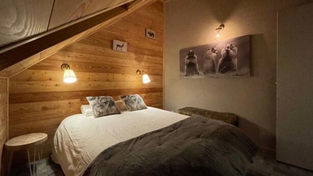 Ein gemütliches Schlafzimmer mit Holzbalkendecke, einem Bett mit weißer Bettdecke, zwei Wandleuchten und einem gerahmten Bild über dem Bett.