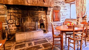 Una chimenea de piedra con repisa de madera, suelo de piedra y una mesa redonda de madera con sillas.