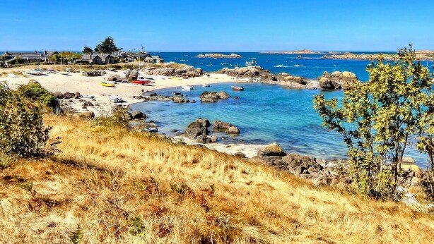 Un paisaje costero con una playa arenosa, costa rocosa y agua azul cristalina.