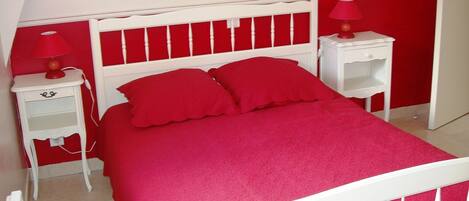 A bedroom with a white bed frame, red bedding, and matching red nightstands with lamps.