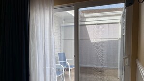Une pièce dotée d’une porte-fenêtre coulissante donnant sur un espace extérieur avec un fauteuil de patio et un mur blanc.
