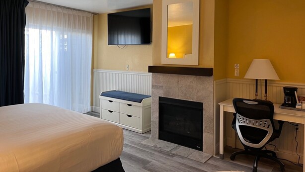 Une chambre d’hôtel comprenant un lit, un bureau avec une chaise, une cheminée, un ventilateur de plafond et un téléviseur fixé au mur.
