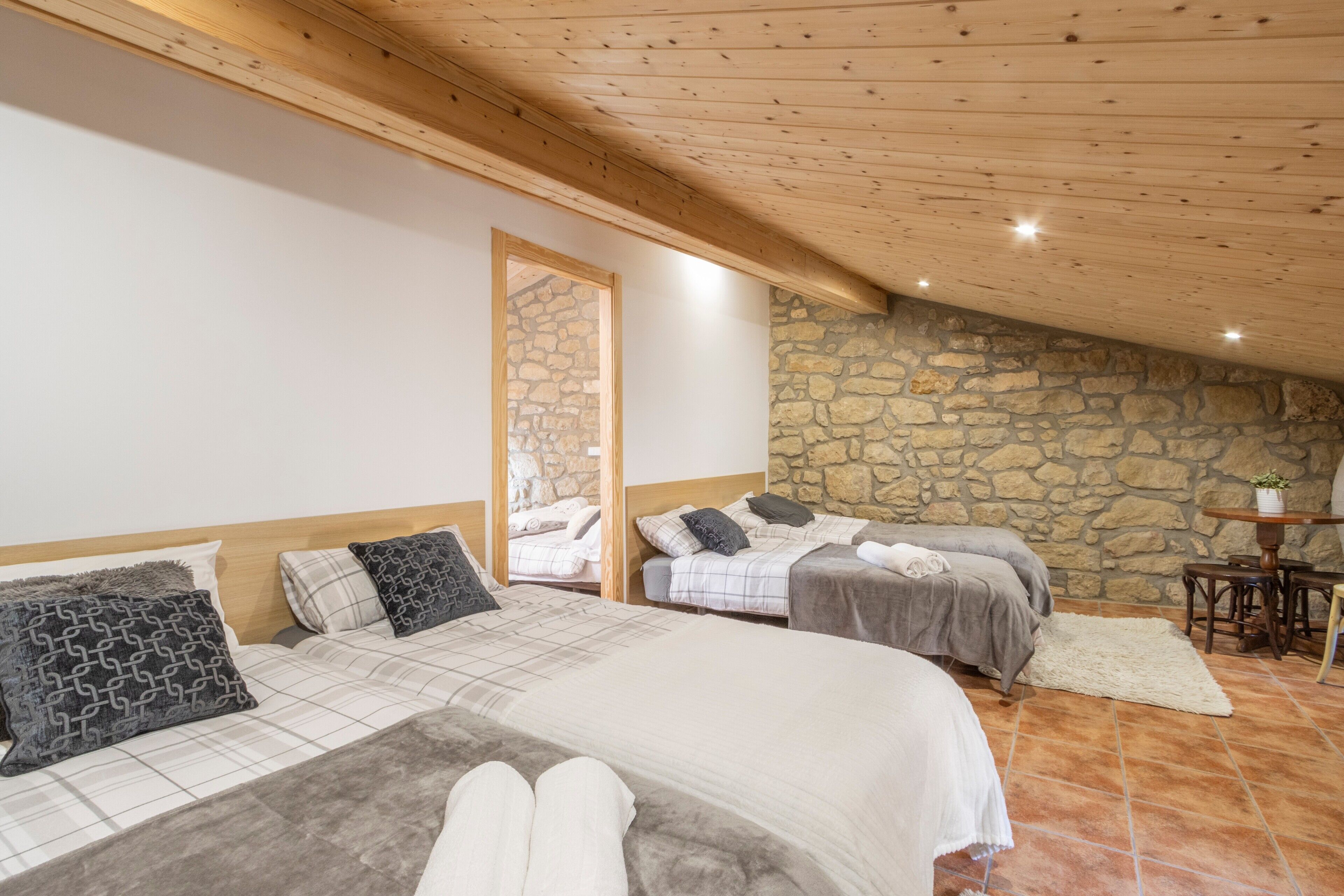 Ein Schlafzimmer mit zwei Betten, Steinwänden, Holzbalkendecke und einem Steinkamin.