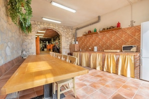 A kitchen with a long wooden table, stone walls, and a tiled backsplash. - Holiday Home 'El Petit Maialenc' with Mountain View and Air Conditioning (Maials)