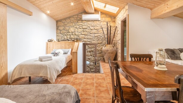 Una habitación acogedora con techo de madera, pared de piedra, una cama, una mesa y un banco.