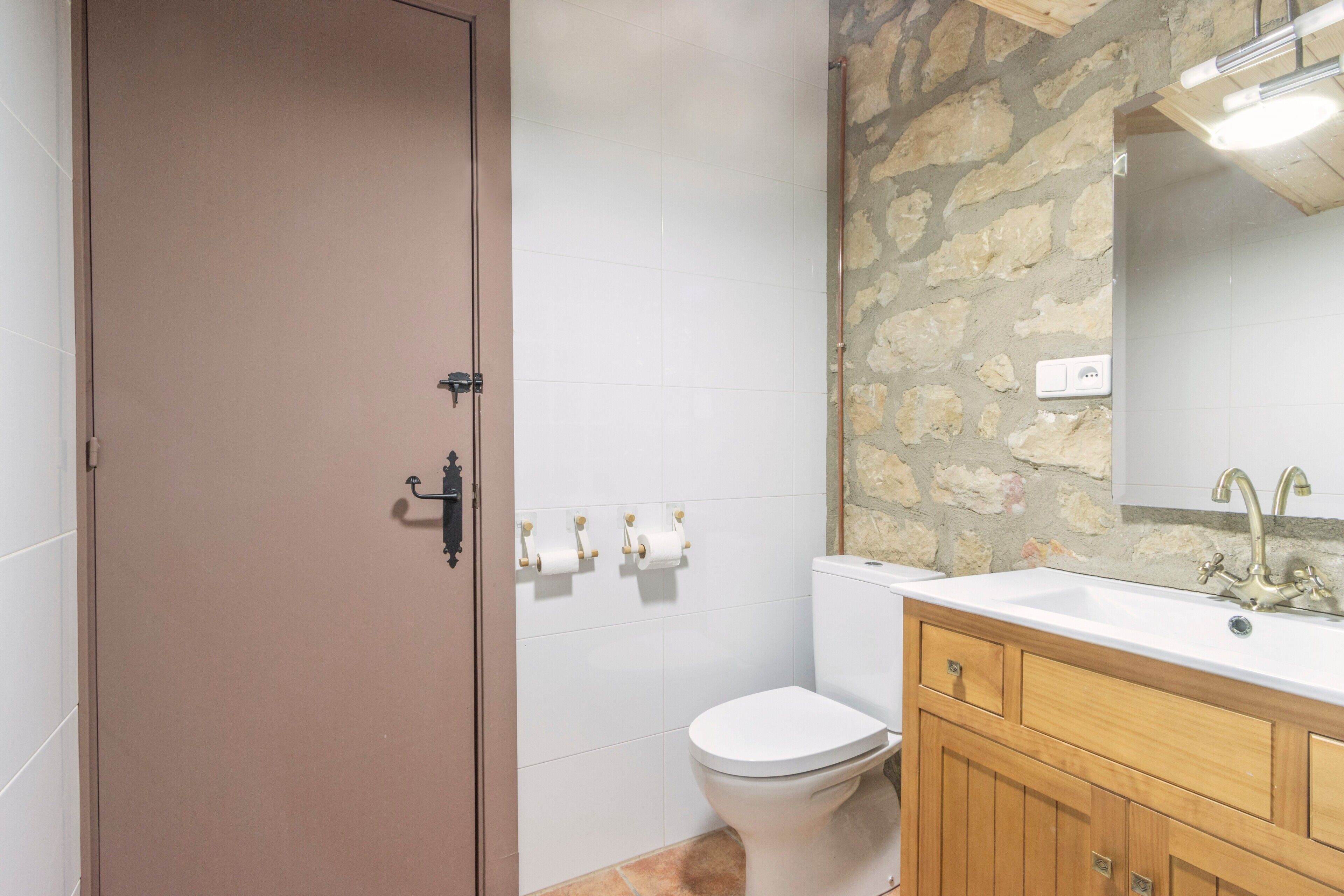 A bathroom with a white toilet, a wooden vanity with a sink, and a stone wall.