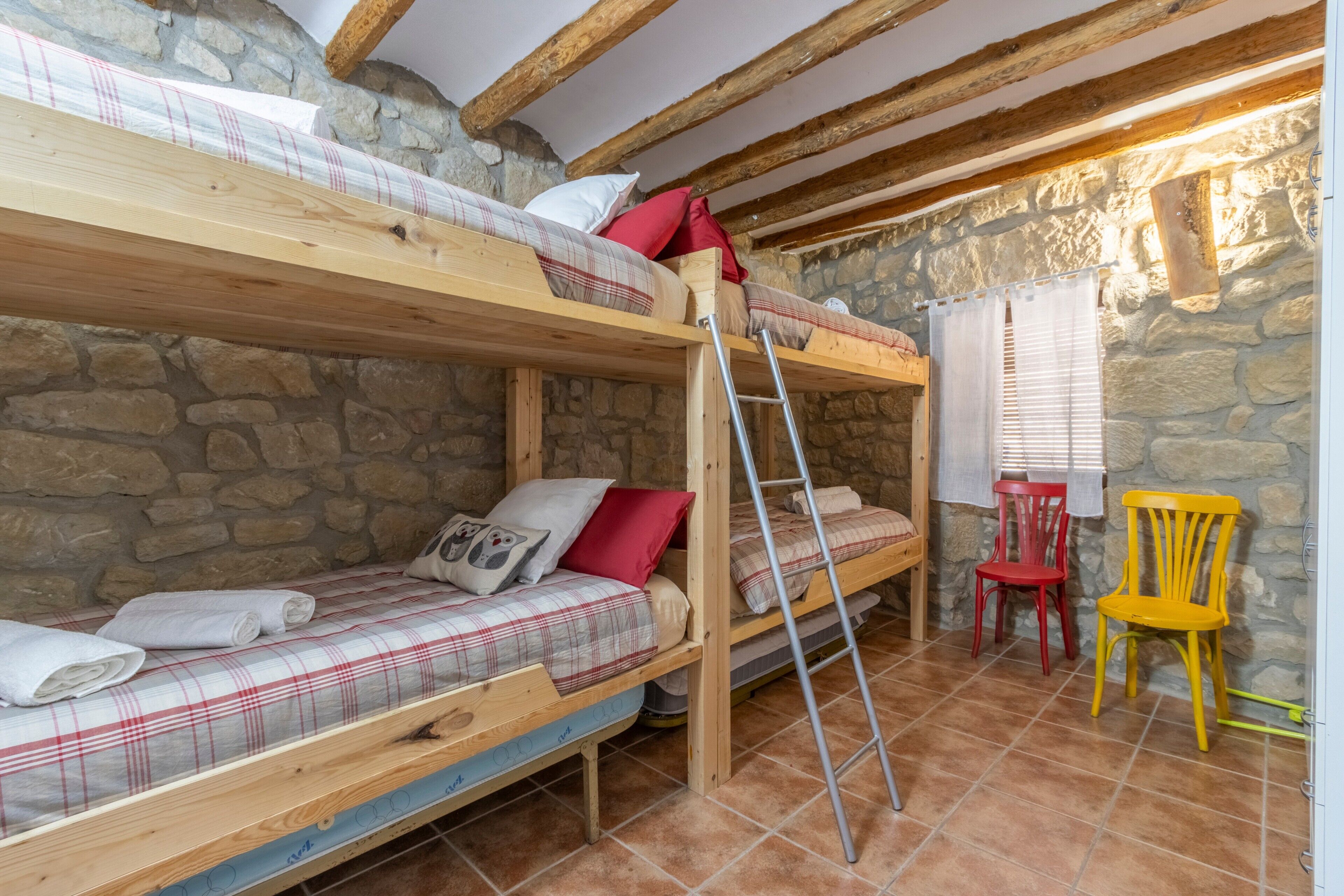 A rustic room with stone walls, wooden bunk beds, a ladder, and a small table with chairs.