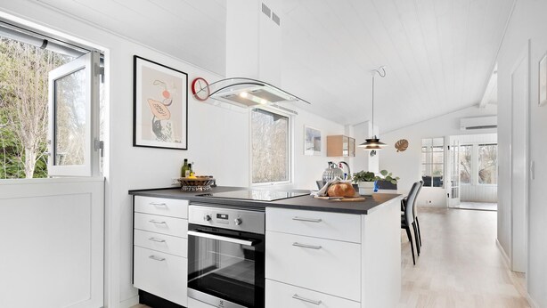 Moderni keittiö, jossa on valkoiset kaapit, sisäänrakennettu uuni ja suuri ikkuna.