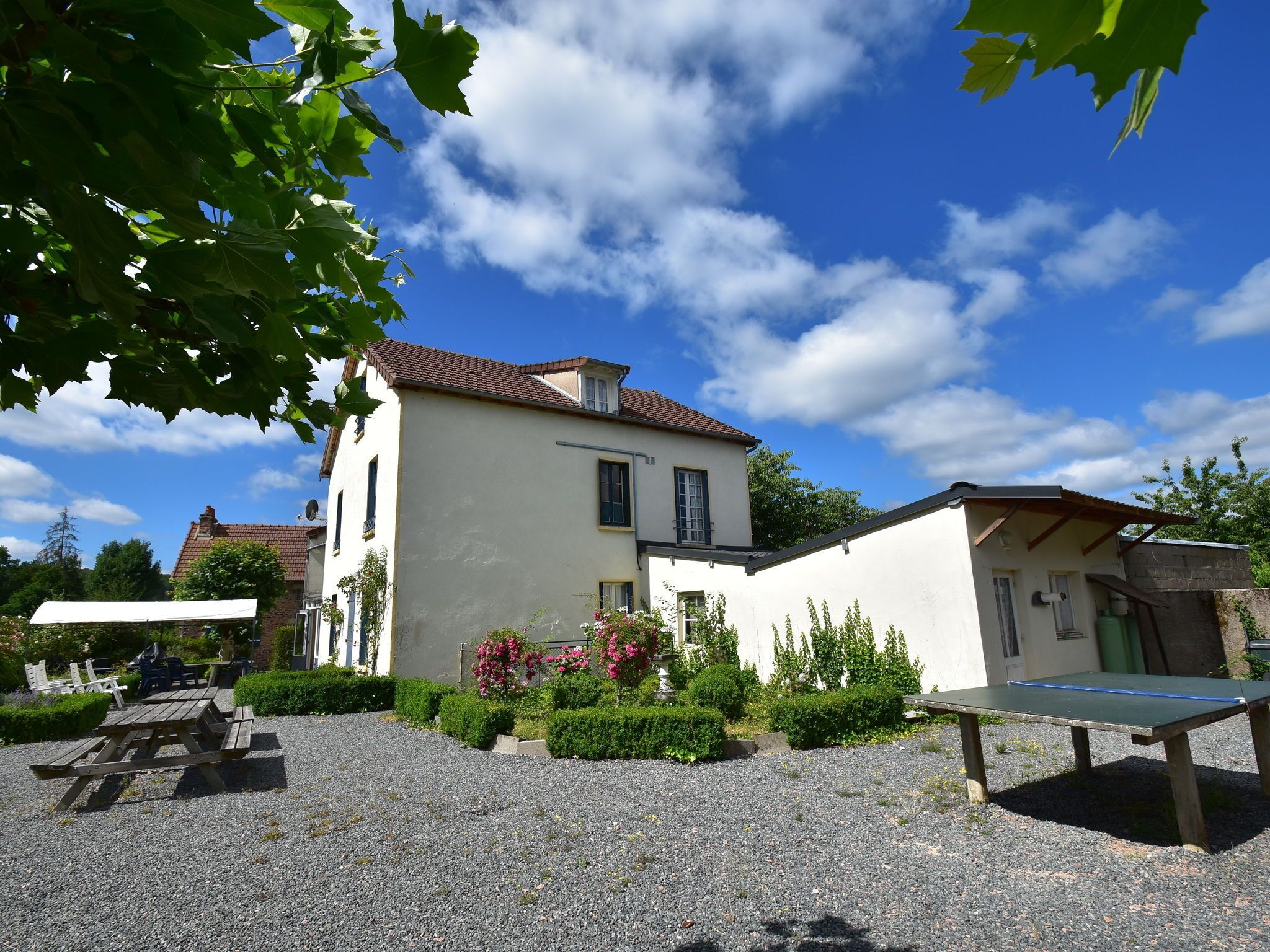 A two-story building with a white exterior and a tiled roof. There is a gravel courtyard with a picnic table and a tennis table.