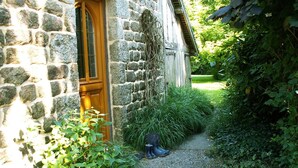 A stone building with a wooden door, surrounded by greenery and a gravel path. - Holiday Home in Ceaucé near Mont Saint Michel (Céaucé)