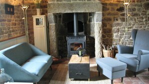 A cozy room with a stone fireplace, two blue armchairs, a small table, and a white cabinet. - Holiday Home in Ceaucé near Mont Saint Michel (Céaucé)