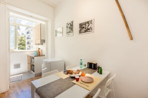 A dining area with a table set for breakfast, a kitchen in the background, and three black-and-white photographs on the wall.