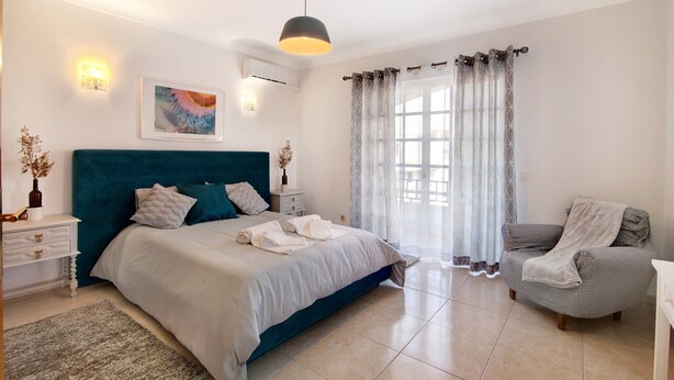 A bedroom with a bed, a chair, a bedside table, a lamp, a painting, and a window with curtains. - Villa 'Casa Judite' with Private Terrace, Balcony and Wi-Fi (Lagoa)