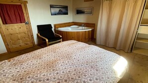 A bedroom with a wooden ceiling, a bed with a floral bedspread, a wooden chair, a wooden bathtub, and a red curtain on a door. - Villa in Ayguatébia-Talau with Garden & BBQ (Ayguatebia-Talau)
