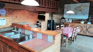A rustic kitchen with wooden beams, a stone wall, a map, and a dining area with wooden chairs and a table. - Villa in Ayguatébia-Talau with Garden & BBQ (Ayguatebia-Talau)