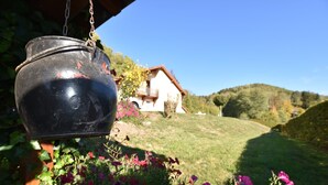 A hanging black pot with a chain, a house with a red roof, and a grassy hill with flowers in the foreground. - Holiday Home in Vosges with Garden and BBQ (Le Haut-Du-Them)