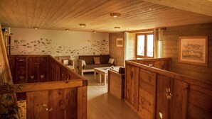 A rustic cabin interior with wooden walls, a stone wall section, a wooden bench, a sofa, and a dining area. - Mansion in Albertville near Ski Slopes (Mercury)