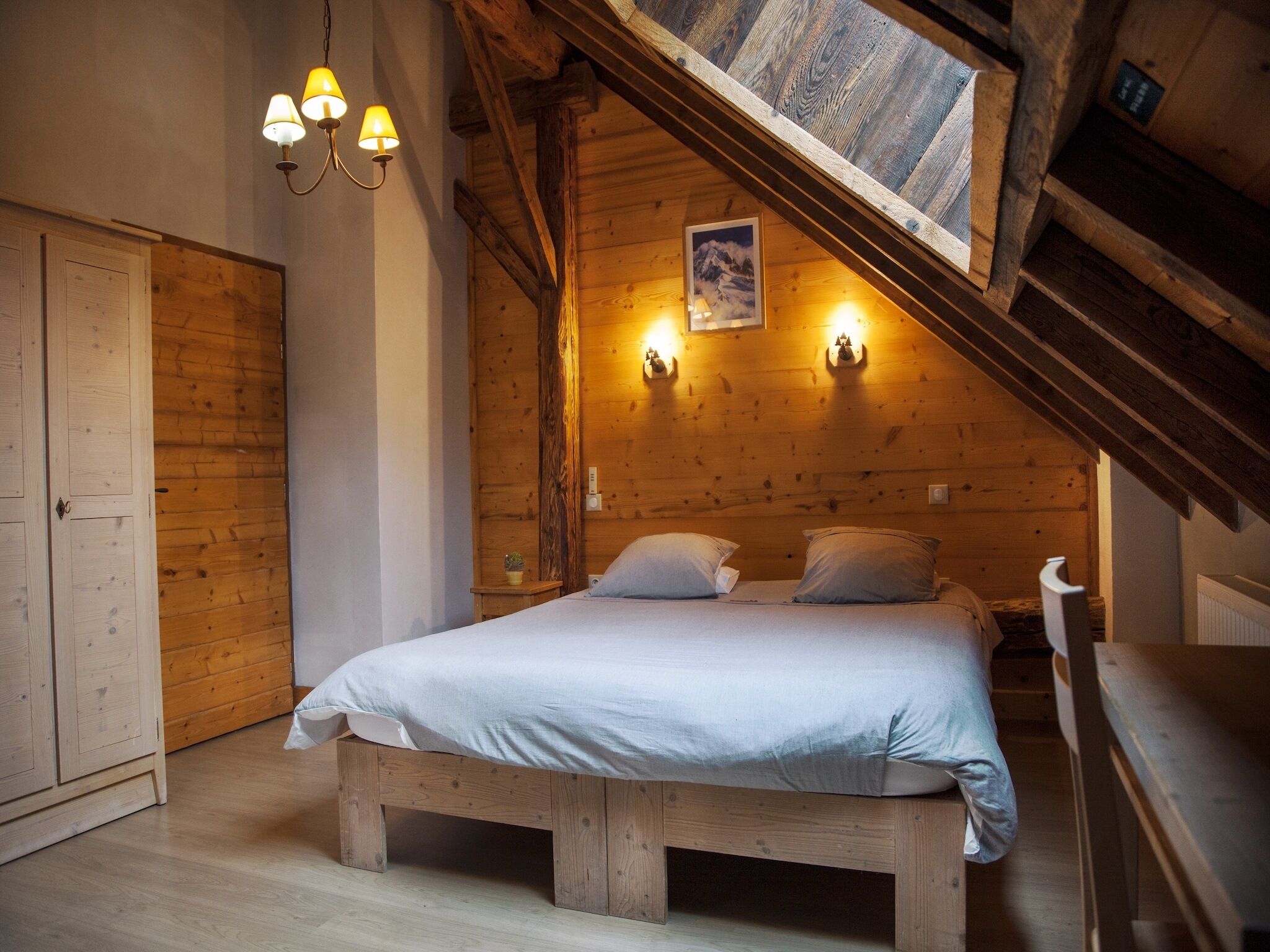 Une chambre confortable avec un lit en bois, une petite table de chevet et un luminaire fixé au mur.