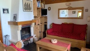 A cozy living room with a fireplace, wooden furniture, and a red patterned sofa. - Chalet in Vallandry near Paradiski Ski Area (Vallandry)