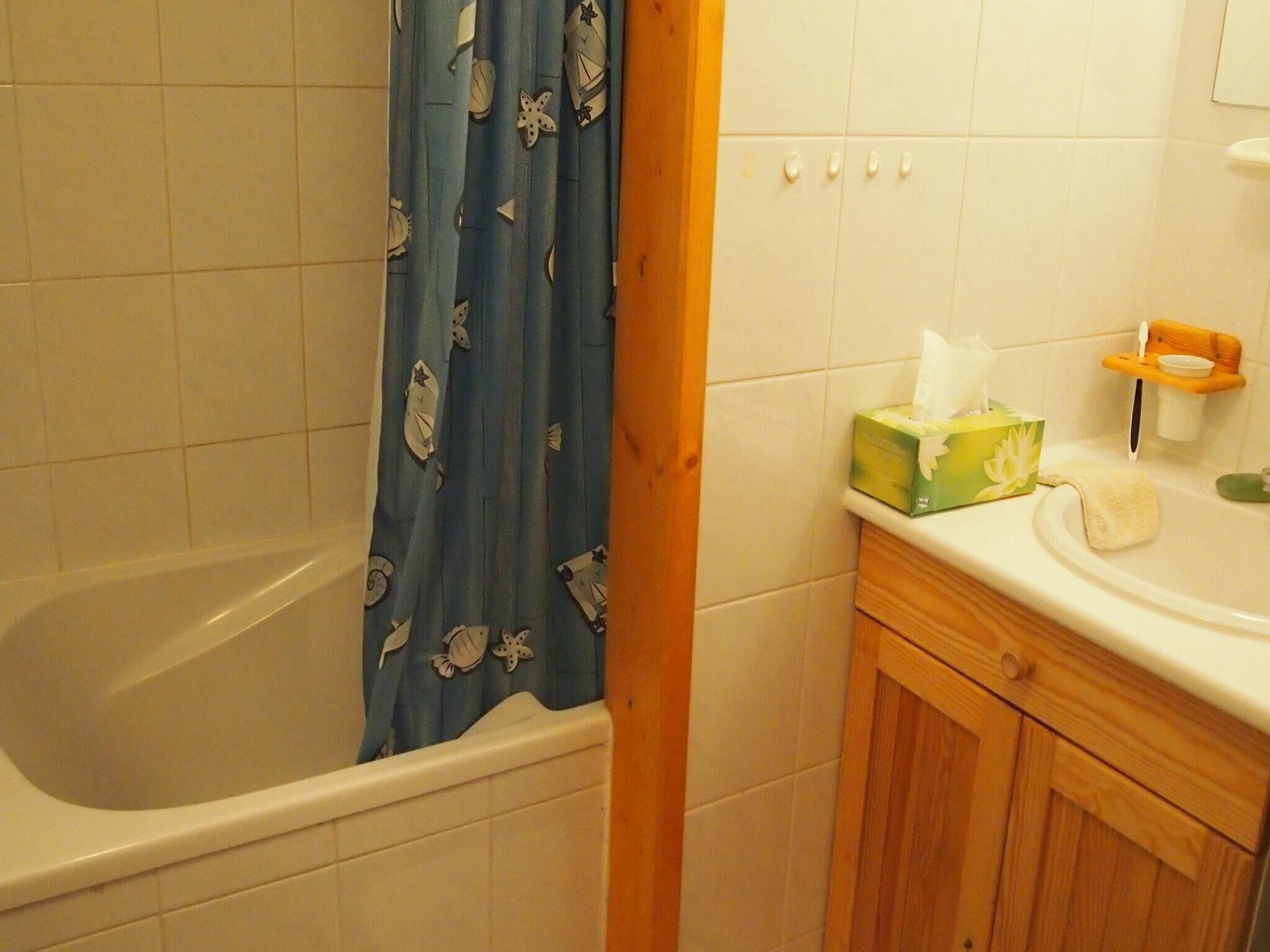 A bathroom with a bathtub, a wooden cabinet, a towel, and a tissue box.