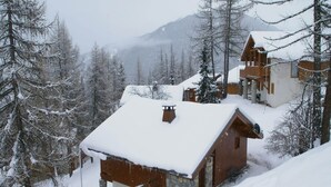 A snow-covered lodge with a stone foundation and wooden exterior, surrounded by snow-laden trees and a mountainous backdrop. - Chalet in Vallandry near Paradiski Ski Area (Vallandry)