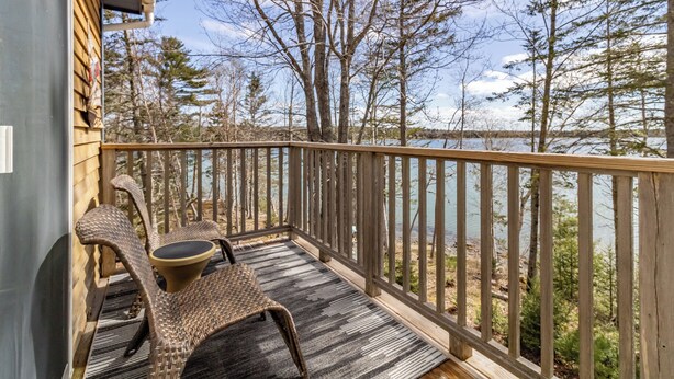 A wooden deck with two wicker chairs and a rug, overlooking a lake with trees and a clear sky. - Private Coveside Escape. Minutes to Acadia (Trenton)