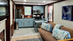 A compact kitchen with wooden cabinets, a dining table, and a sofa with patterned cushions.
