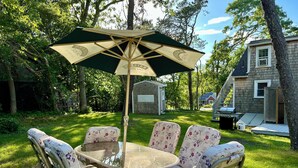A round glass table with floral chairs and a green umbrella.