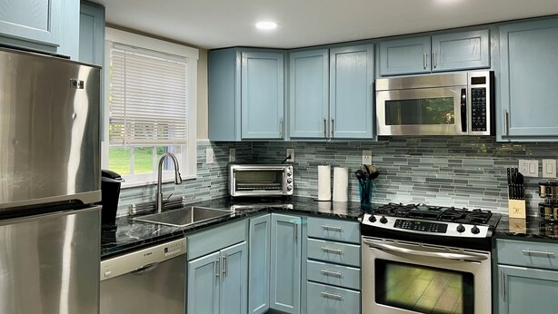A modern kitchen with stainless steel appliances, light blue cabinets, and a tiled backsplash.