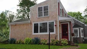 A two-story house with a red door, large windows, and a well-maintained front yard with various plants.