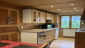 A wooden cabin-style kitchen with a wooden table and chairs, a sink, stove, and cabinets. - Chalet in Notre-Dame near Ski Lift (Notre Dame de Bellecombe)