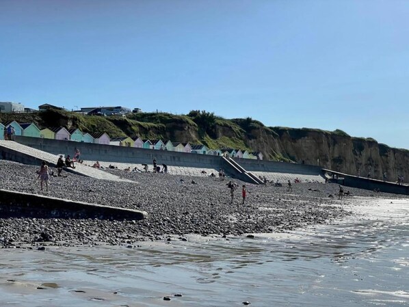 Una playa pedregosa con gente y cabañas de playa coloridas al fondo.