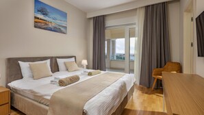 Une chambre d’hôtel avec un grand lit, un bureau, une chaise, un balcon avec des rideaux et un tableau au mur.