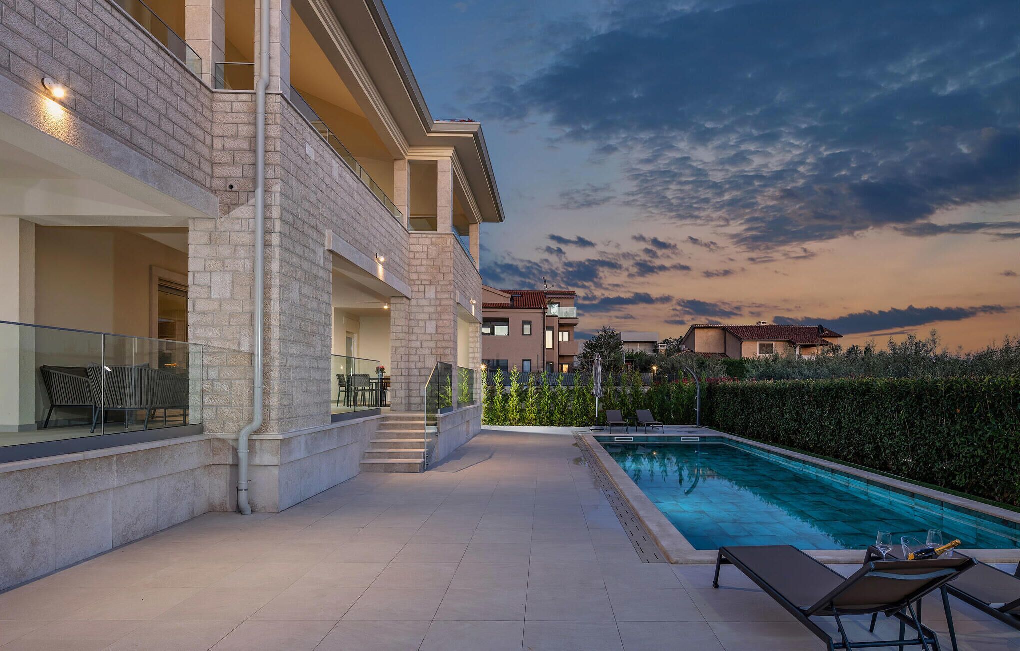 A modern building with a swimming pool, outdoor seating, and a view of neighboring houses.