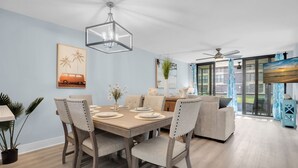 A dining area with a wooden table and chairs, a ceiling fan, and a view of the outdoors through large windows.