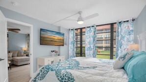 A bedroom with a bed, a ceiling fan, a painting, and a window with curtains.