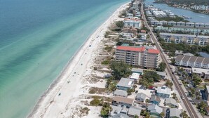 An aerial view of a coastal area with a beach, buildings, and a road.