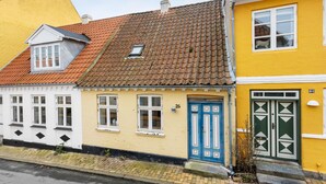 En rad färgglada byggnader med distinkta arkitektoniska stilar, bland annat en gul byggnad med en blå dörr och en vit byggnad med svarta, diamantformade mönster.