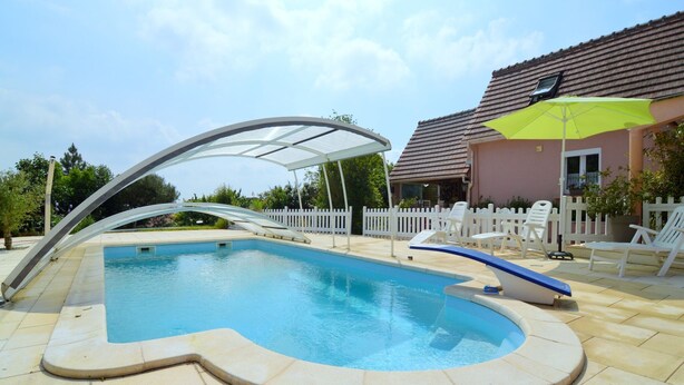 Ein Pool mit gewölbter Kante, einem überdachten Bereich und einem weißen Zaun im Hintergrund.