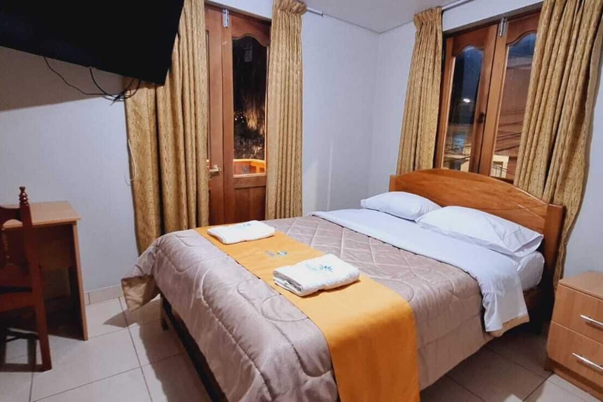 A bedroom with a bed, a wooden chair, a nightstand, and curtains.