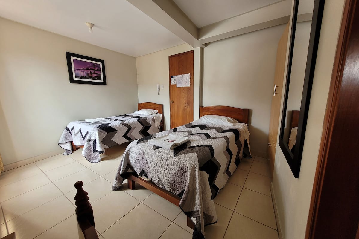 A room with two beds, a wooden door, a framed picture on the wall, and a mirror on the right.