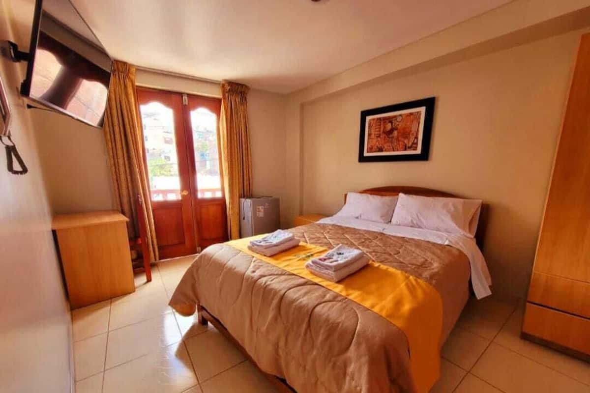 A hotel room with a bed, a television, a desk, and a door with curtains.