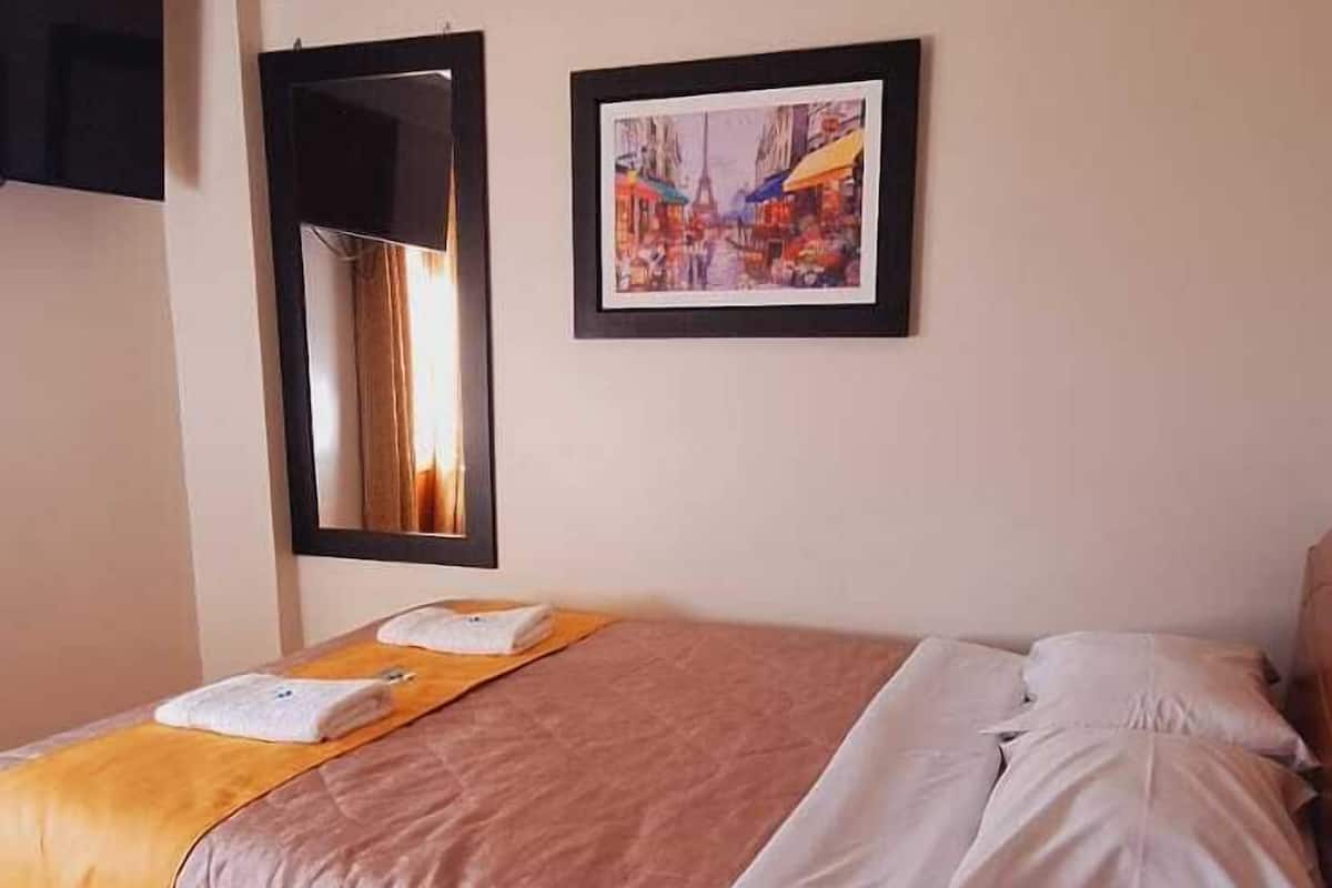 A hotel room with a bed, a framed picture on the wall, and a window with curtains.