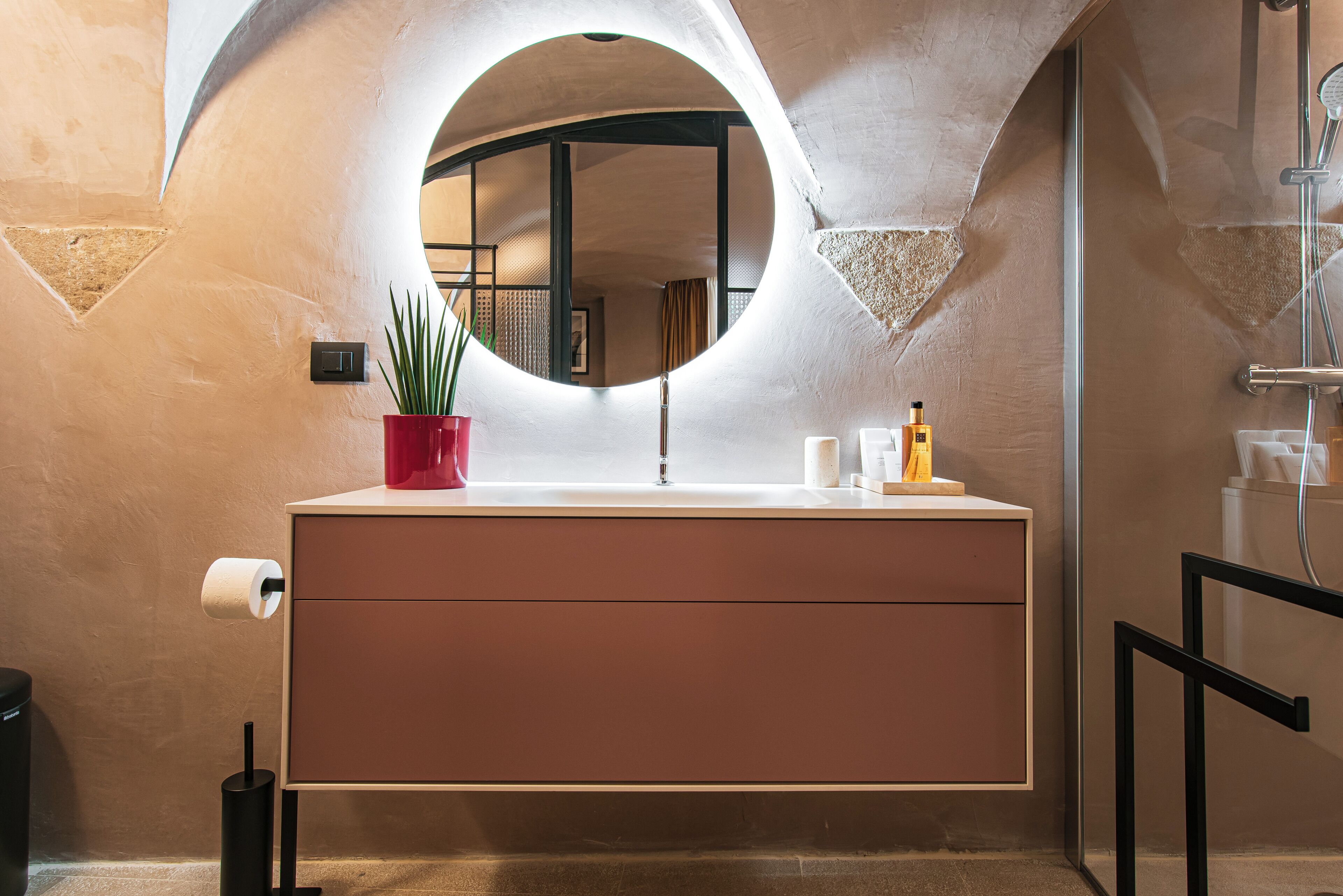 Une salle de bain avec un miroir rond, un lavabo et une plante en pot.