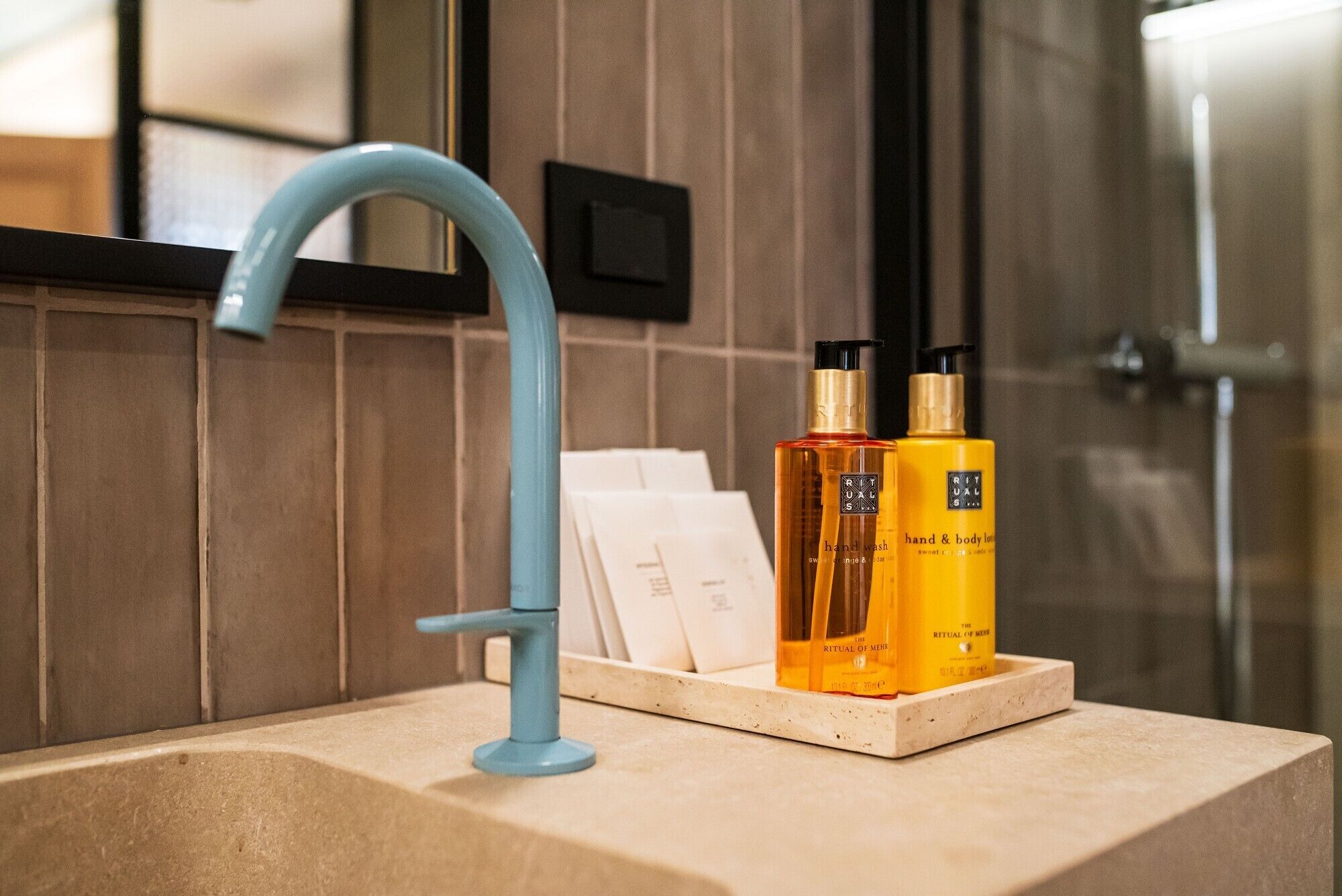 A bathroom with a blue faucet, a wooden vanity, and two bottles of hand and body lotion on the counter.